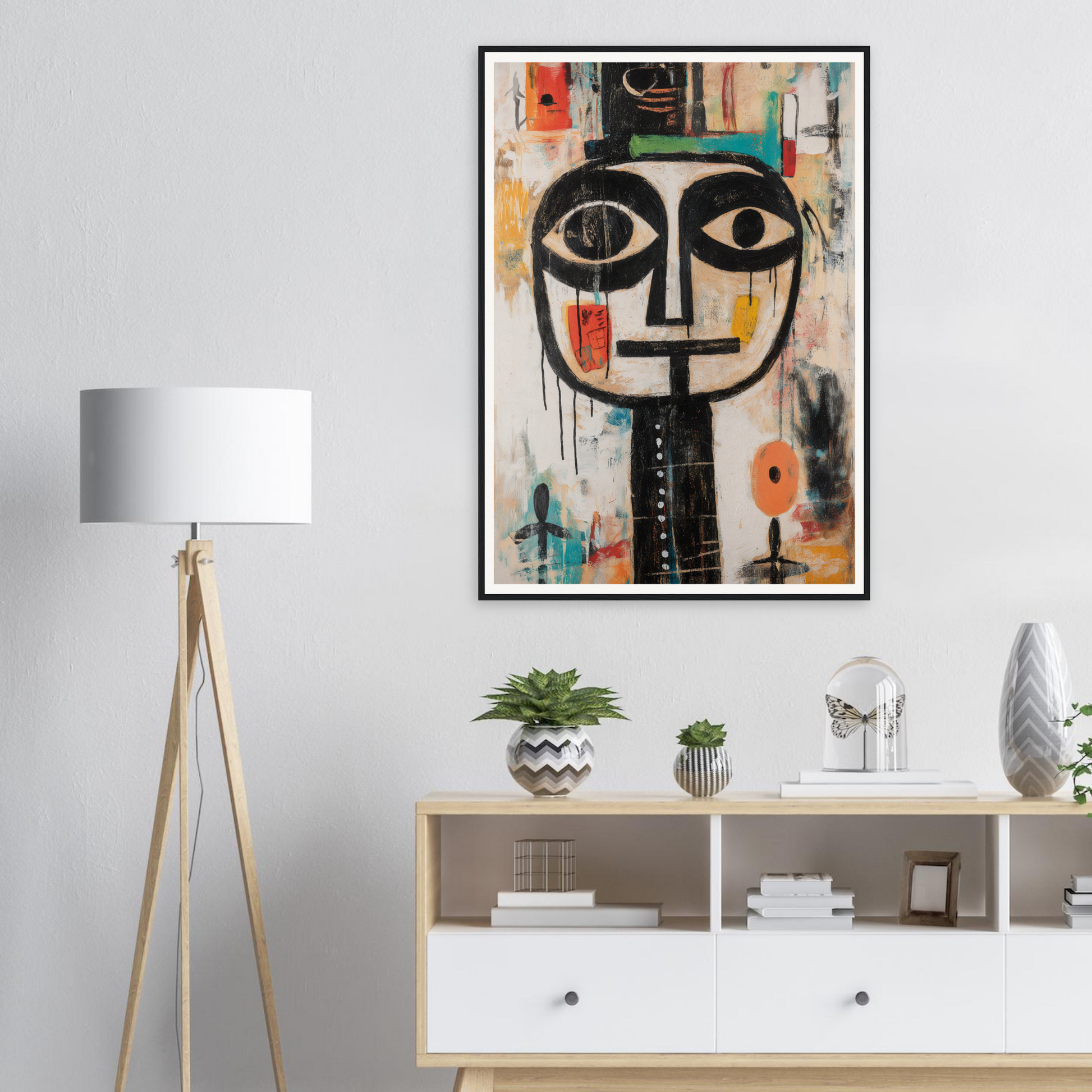 Framed wall art of an abstract face sits above a shelf, next to a floor lamp.