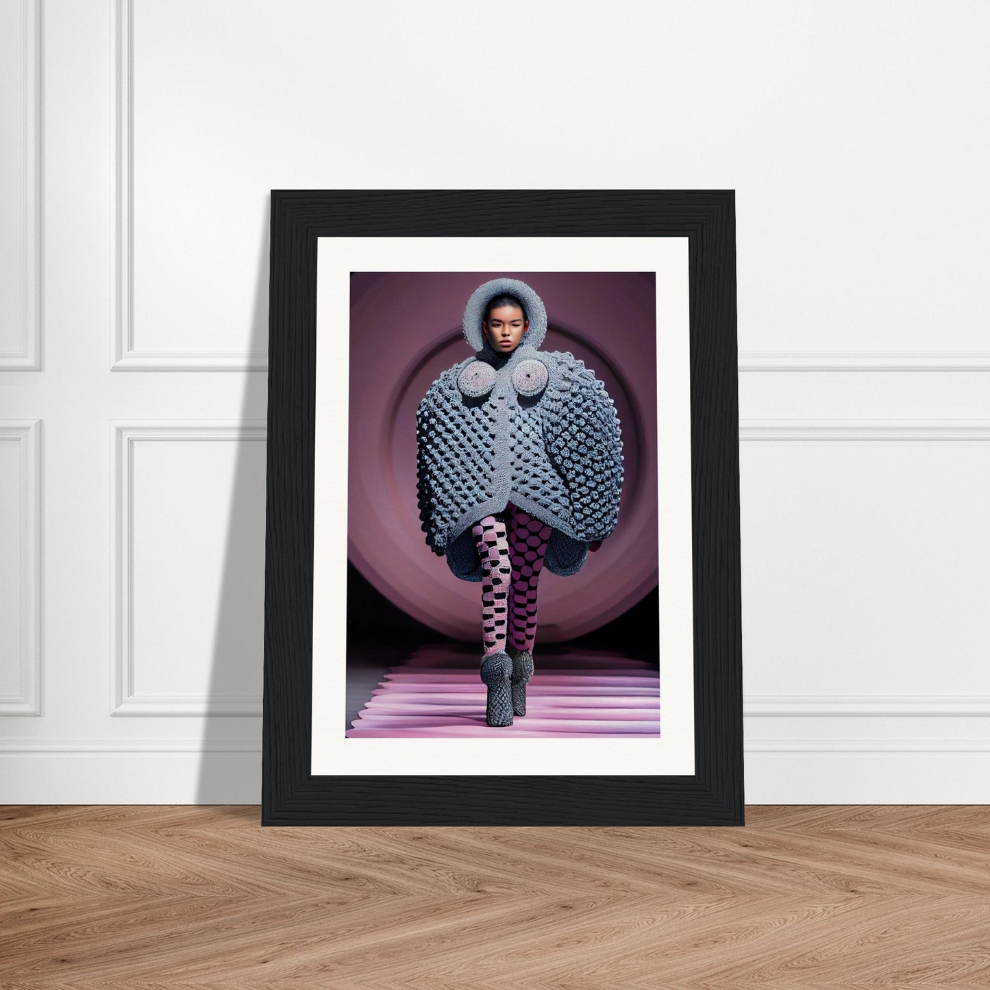 Framed photograph of a fashion model wearing an oversized quilted coat and patterned tights on a pink runway.