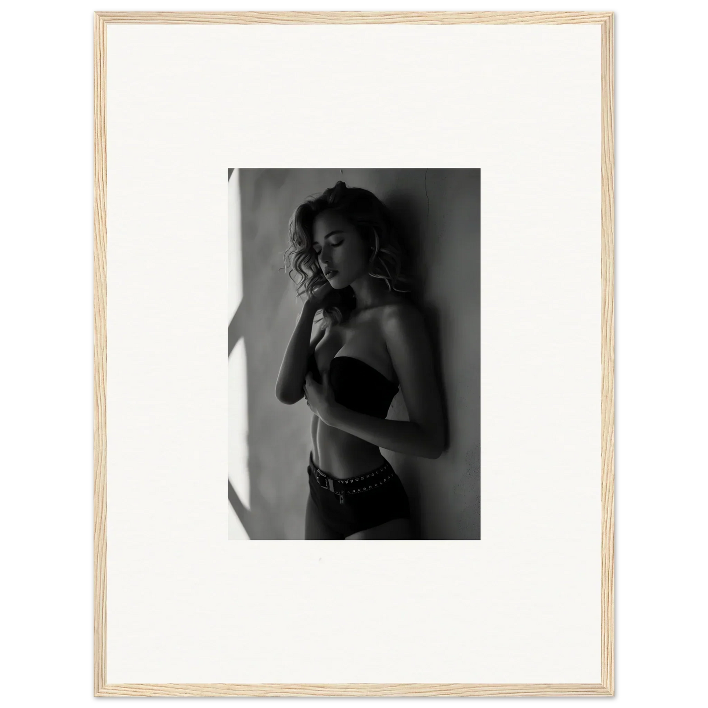 Black and white photograph of a woman in lingerie posing against a wall.