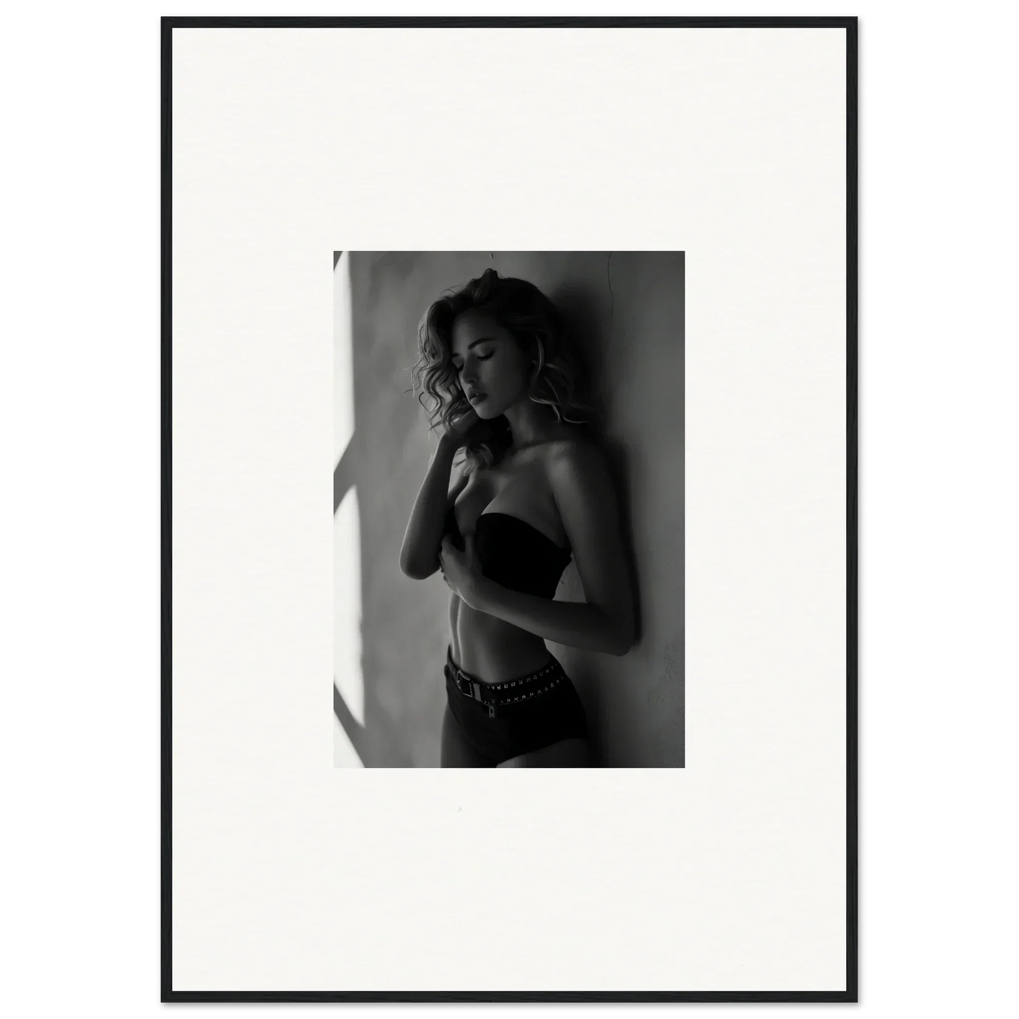 Black and white photograph of a woman in lingerie posing against a wall.