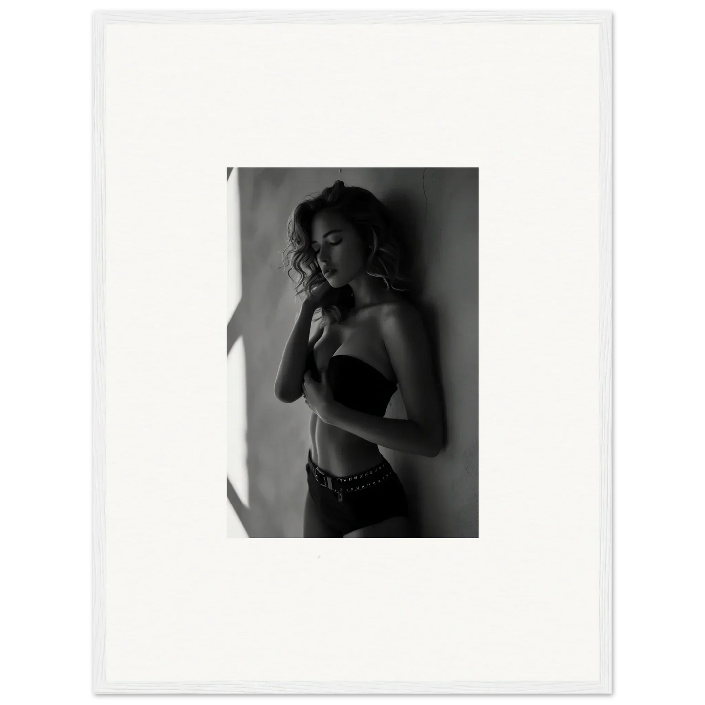 Black and white photograph of a woman in lingerie posing against a wall.