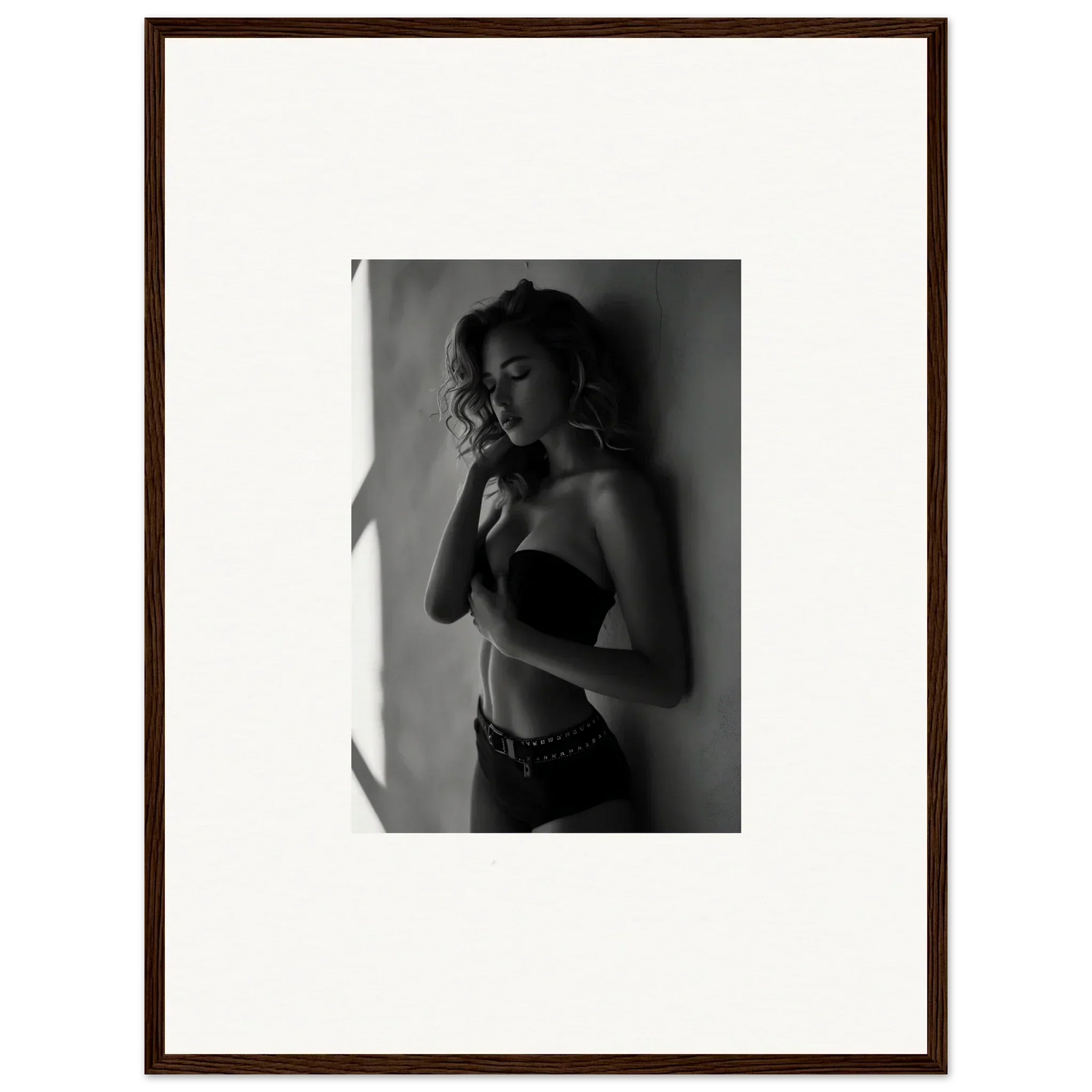 Black and white photograph of a woman in a strapless top posing against a wall.