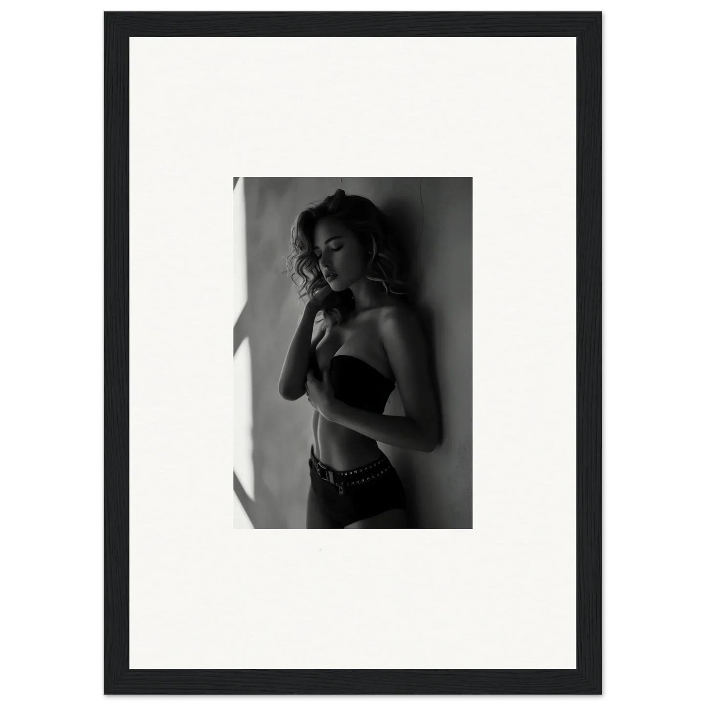 Black and white photograph of a woman in lingerie posing against a wall.
