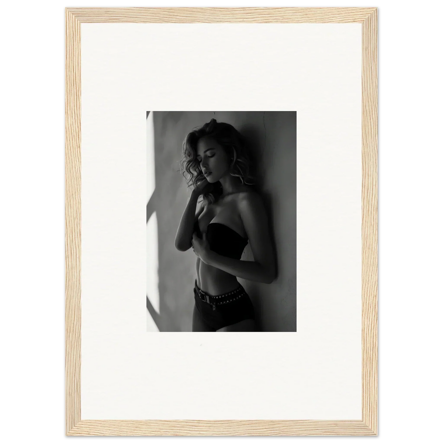 Black and white photograph of a woman in a bra and low-rise pants, posing with one hand near her face.