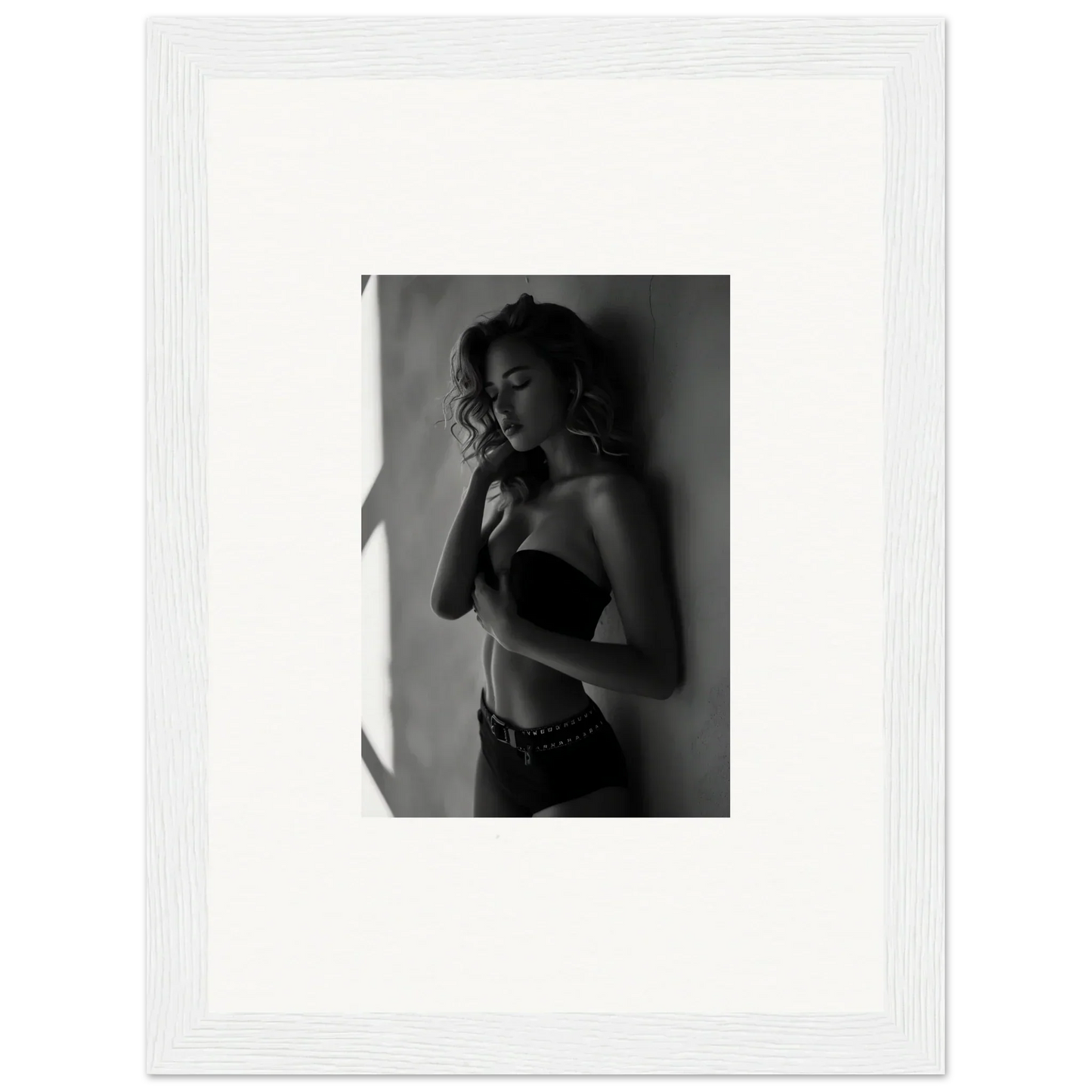 Black and white photograph of a woman in lingerie posing against a wall.