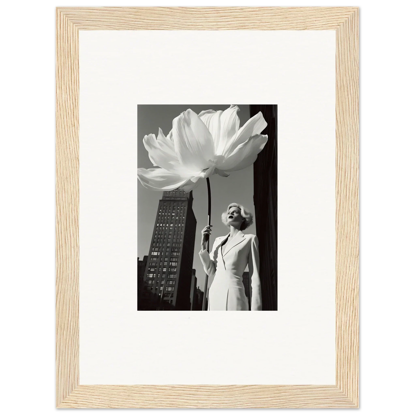Framed black and white photograph showing a person holding an oversized flower next to a tall building.