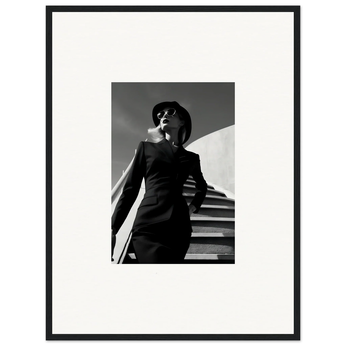 Black and white photograph of a stylishly dressed woman in sunglasses and a hat.