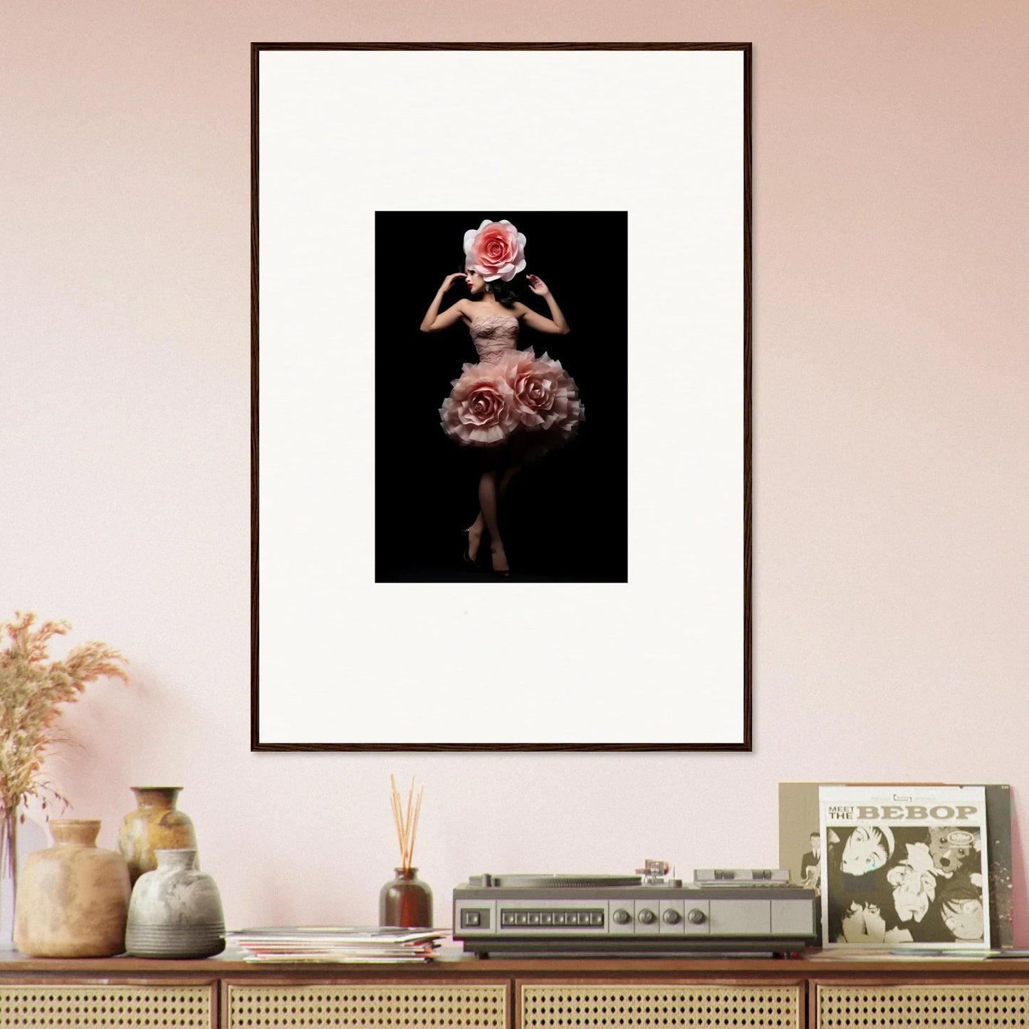 Framed artwork depicting a figure with a rose-like head wearing a floral skirt against a dark background.