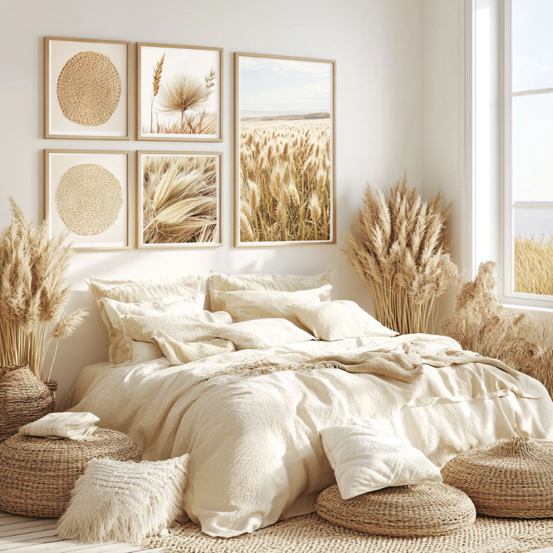 A bright bedroom features a cozy bed with fluffy pillows and blankets. The room is decorated with framed nature artwork, woven baskets, and pampas grass, creating a warm and inviting atmosphere. Large windows offer natural light.