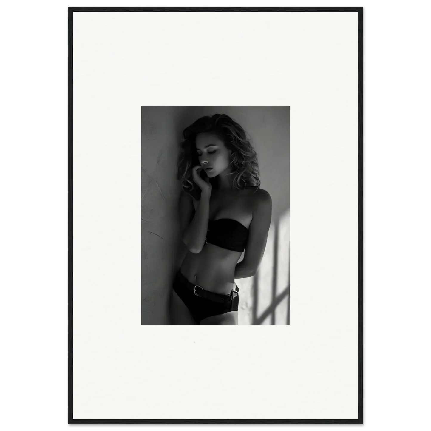 Black and white photograph of a woman in lingerie posing against a wall.