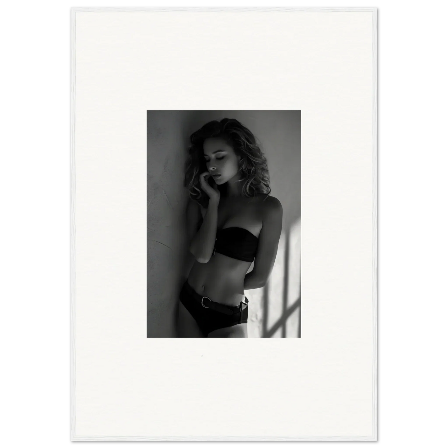 Black and white photograph of a woman in lingerie posing against a wall.