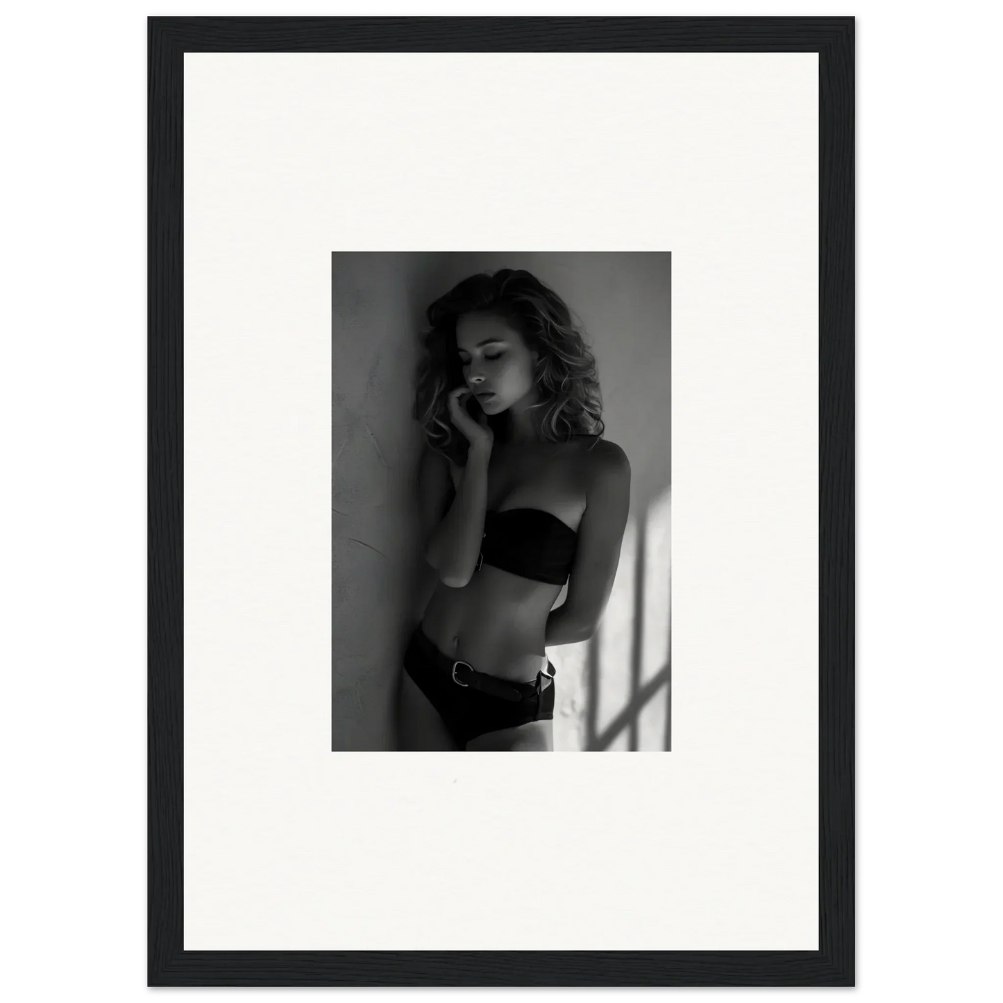 Black and white photograph of a woman in lingerie posing against a wall.