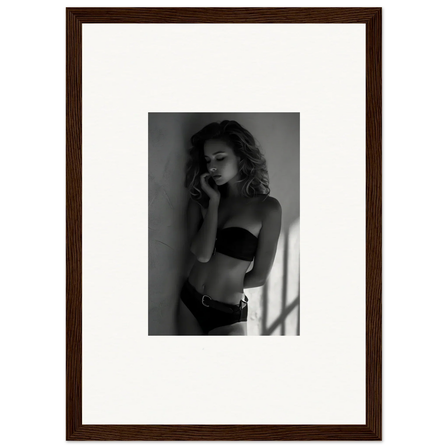 Black and white photograph of a woman in lingerie posing against a wall.