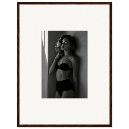 Black and white photograph of a woman in lingerie posing against a wall.