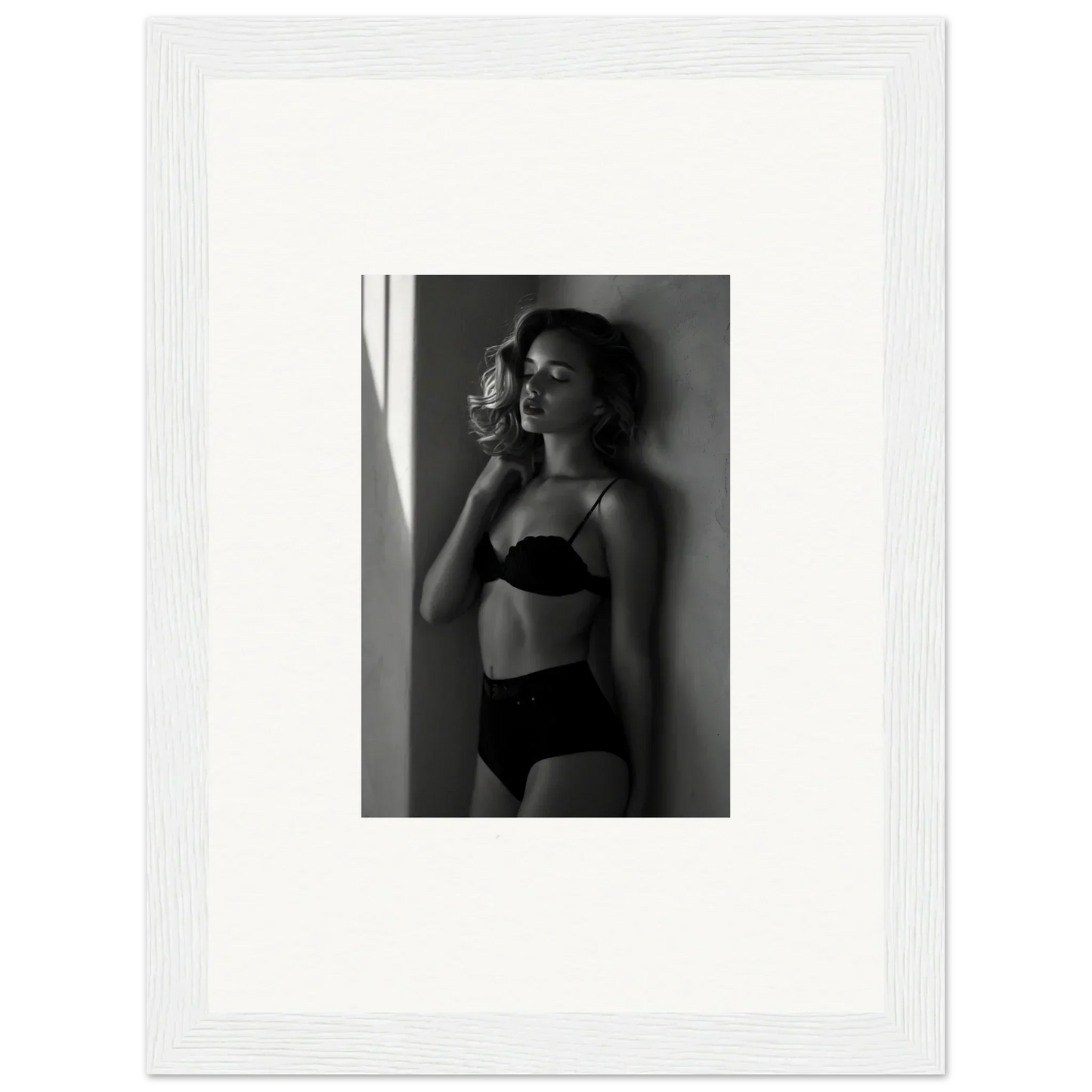 Black and white photograph of a woman in lingerie posing against a wall.