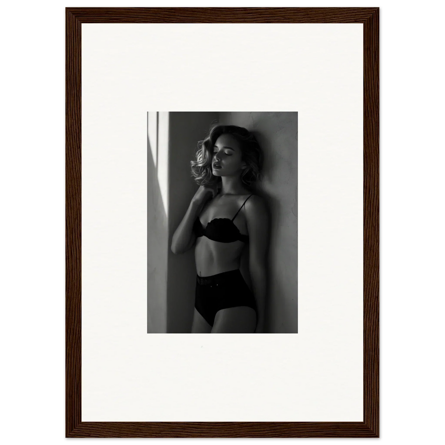 Black and white photograph of a woman in lingerie posing against a wall.