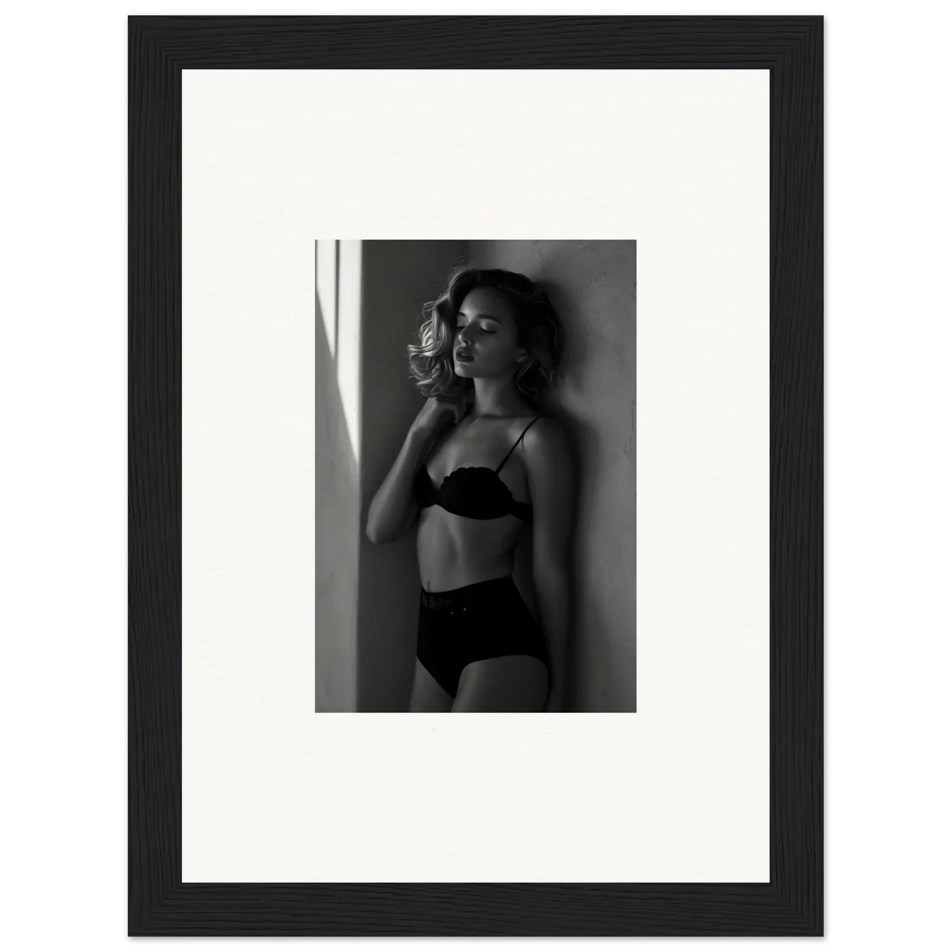 Black and white photograph of a woman in lingerie posing against a wall.