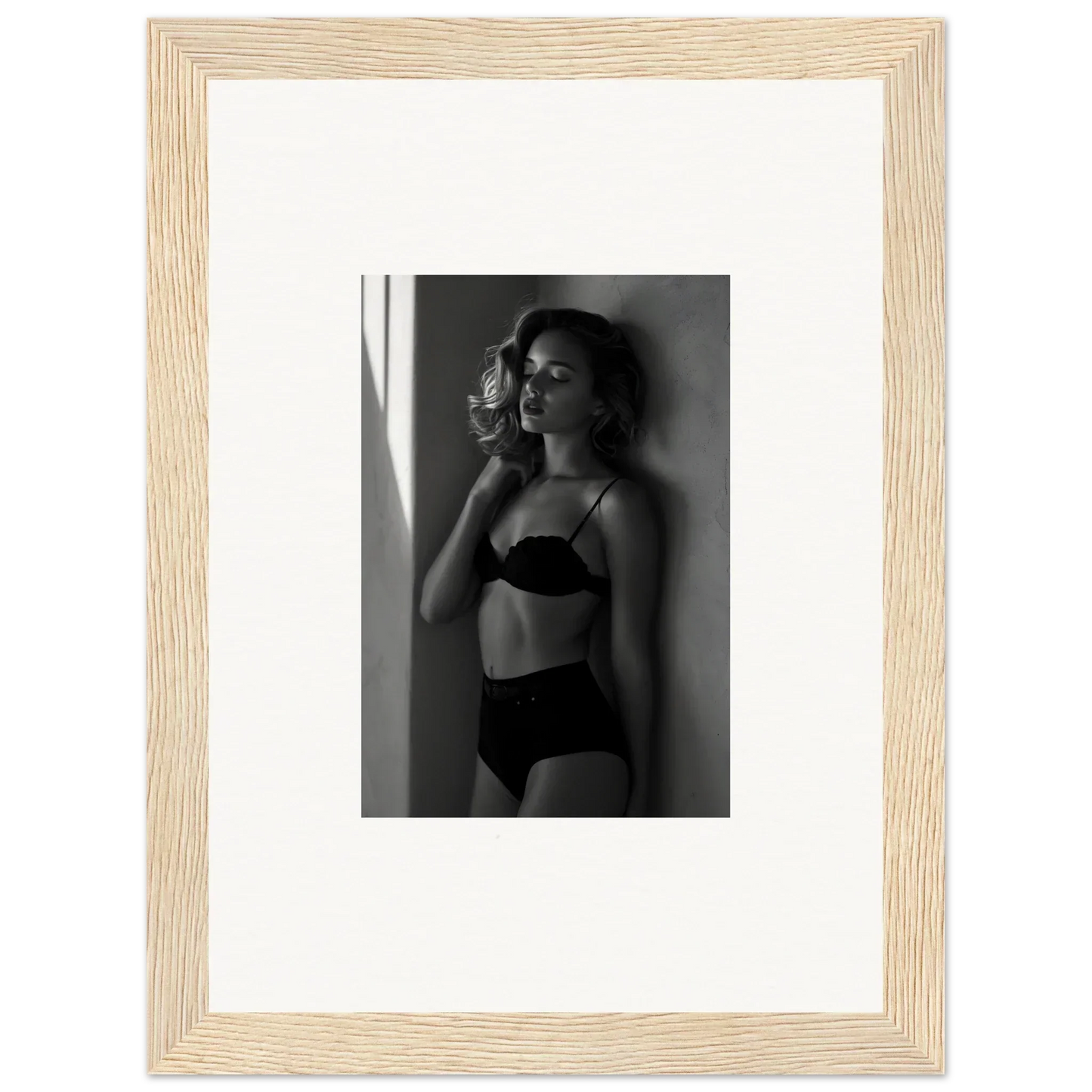 Black and white photograph of a woman in lingerie posing against a wall.