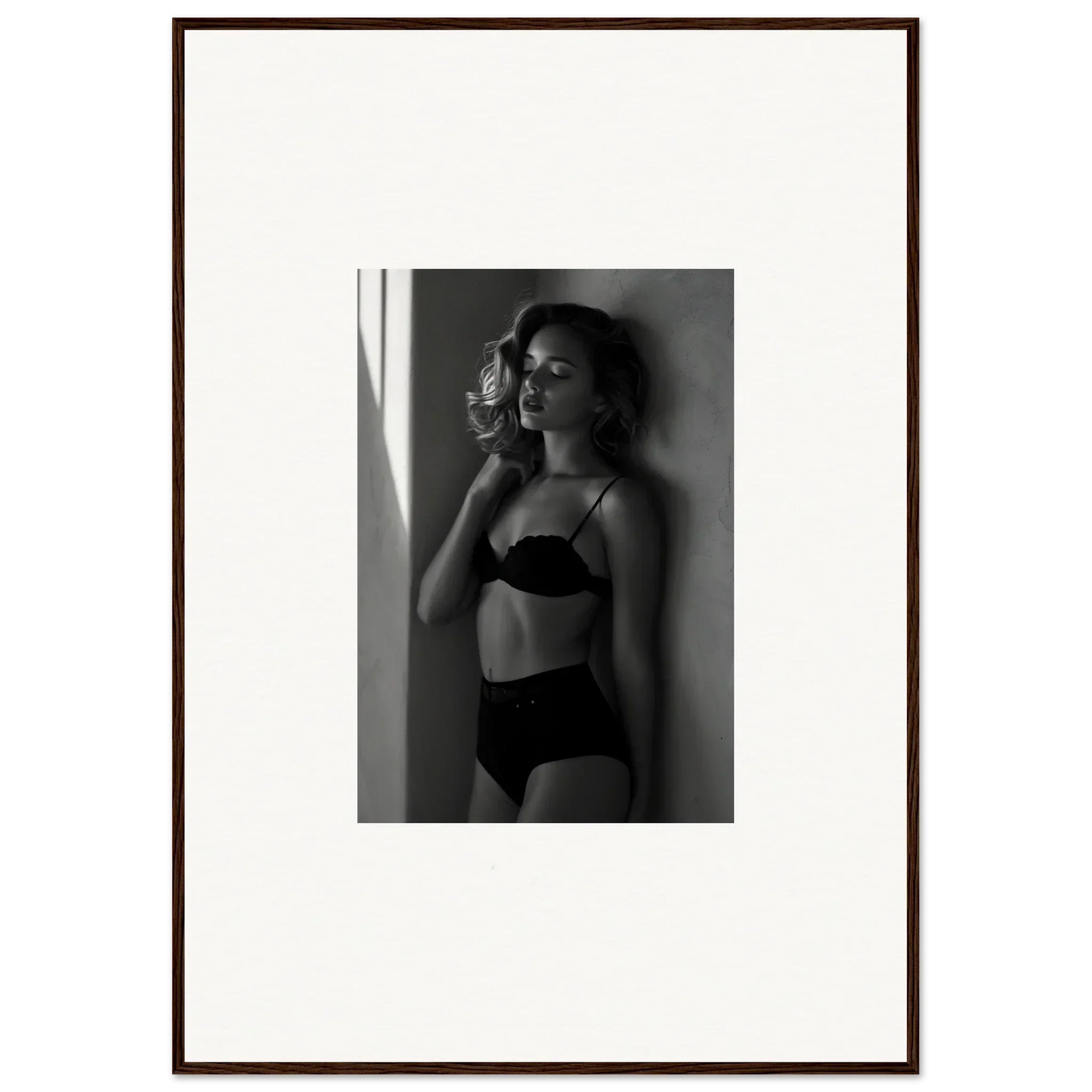 Black and white photograph of a woman in lingerie posing against a wall.