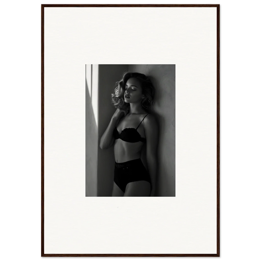 Black and white photograph of a woman in lingerie posing against a wall.