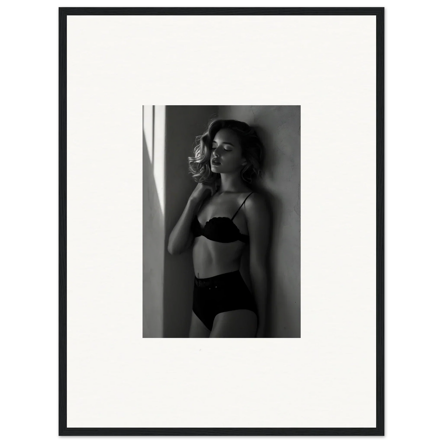 Black and white photograph of a woman in lingerie posing against a wall.