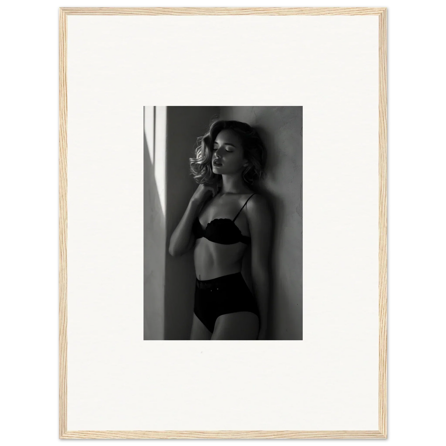 Black and white photograph of a woman in lingerie posing against a wall.