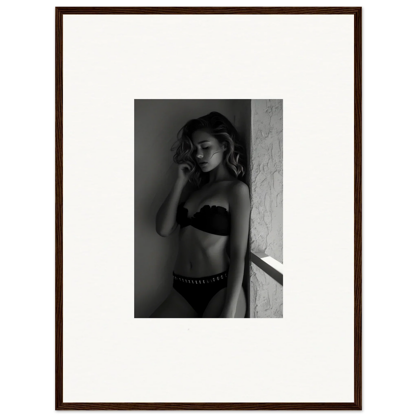 Black and white photograph of a woman in lingerie posing against a wall.