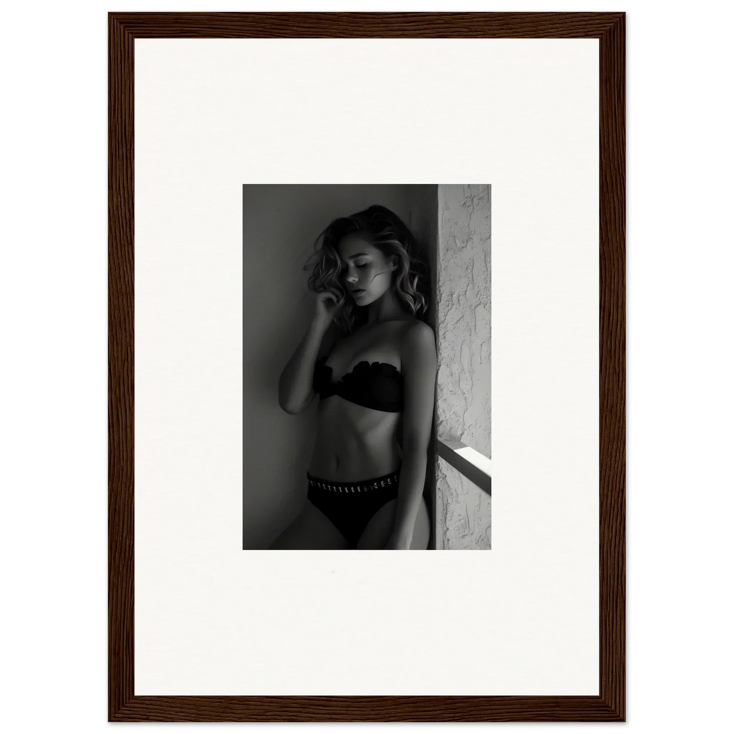 Black and white photograph of a woman in lingerie posing against a wall.