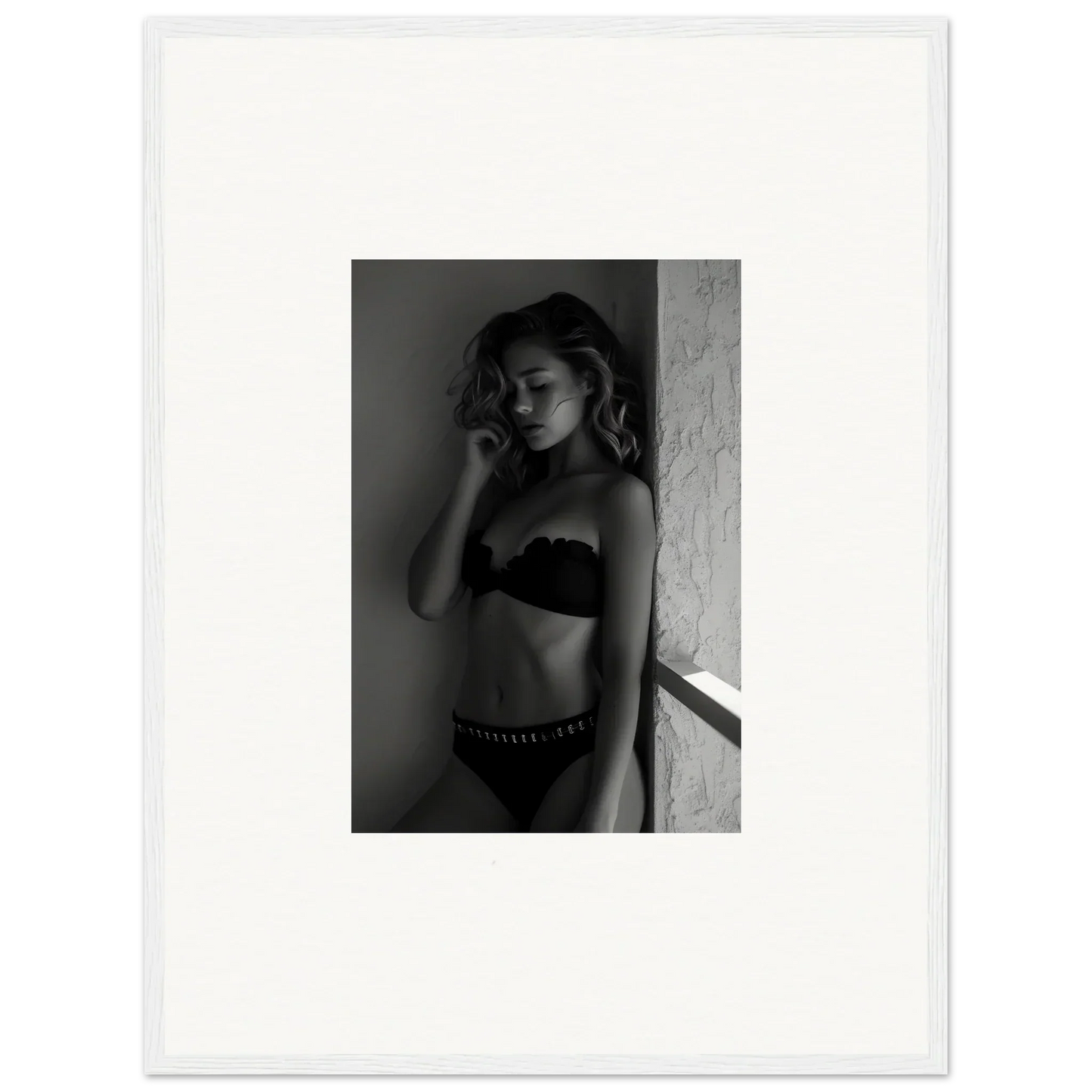 Black and white photograph of a woman in lingerie posing against a wall.