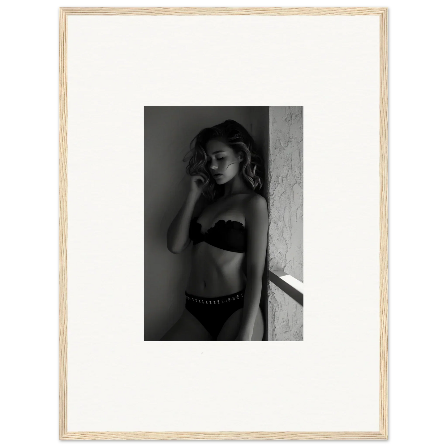 Black and white photograph of a woman in lingerie posing against a wall.