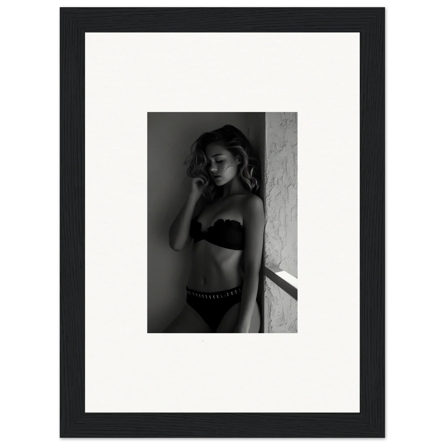 Black and white photograph of a woman in lingerie leaning against a wall.