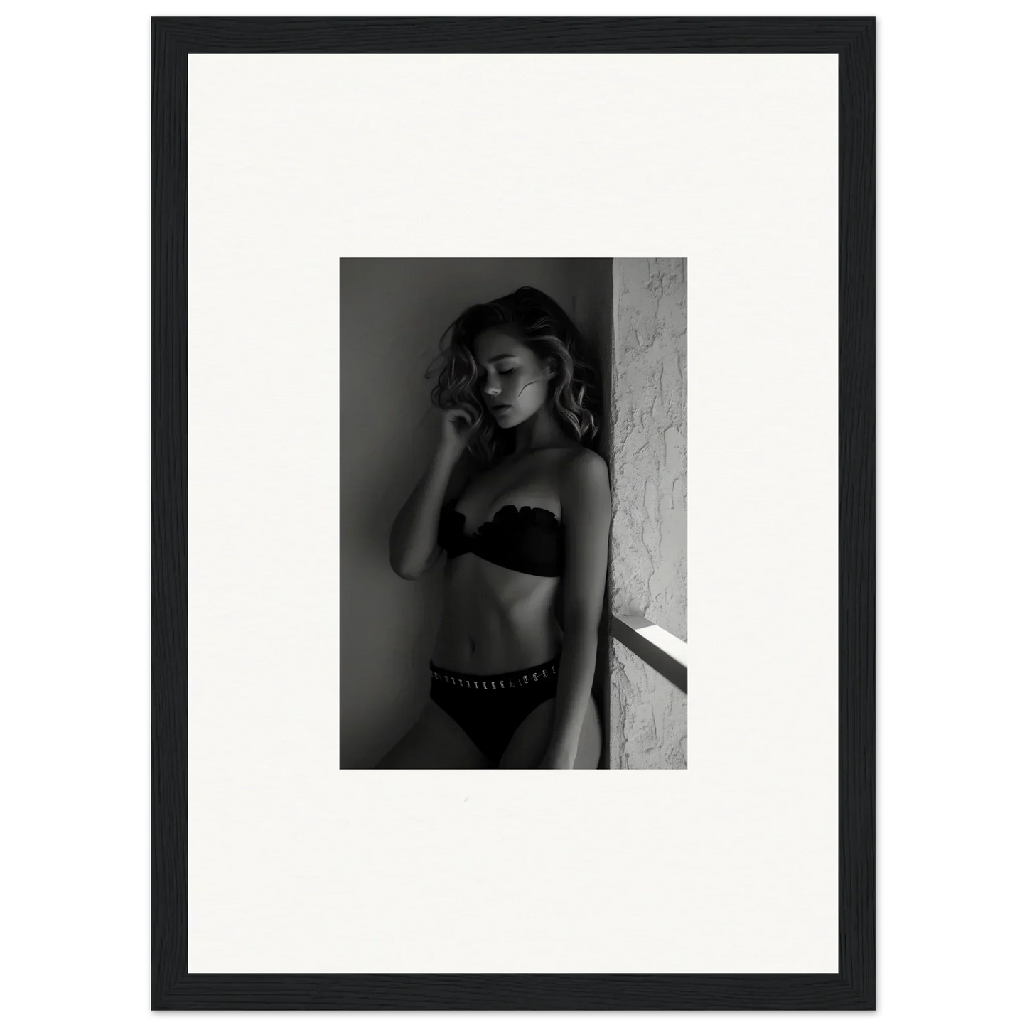 Black and white photograph of a woman in lingerie leaning against a wall.