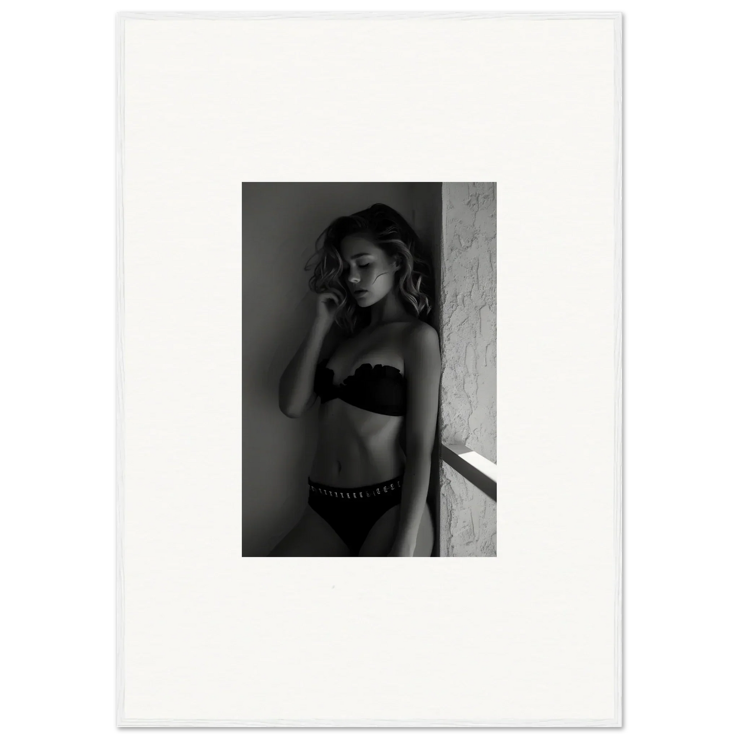 Black and white photograph of a woman in lingerie leaning against a wall.