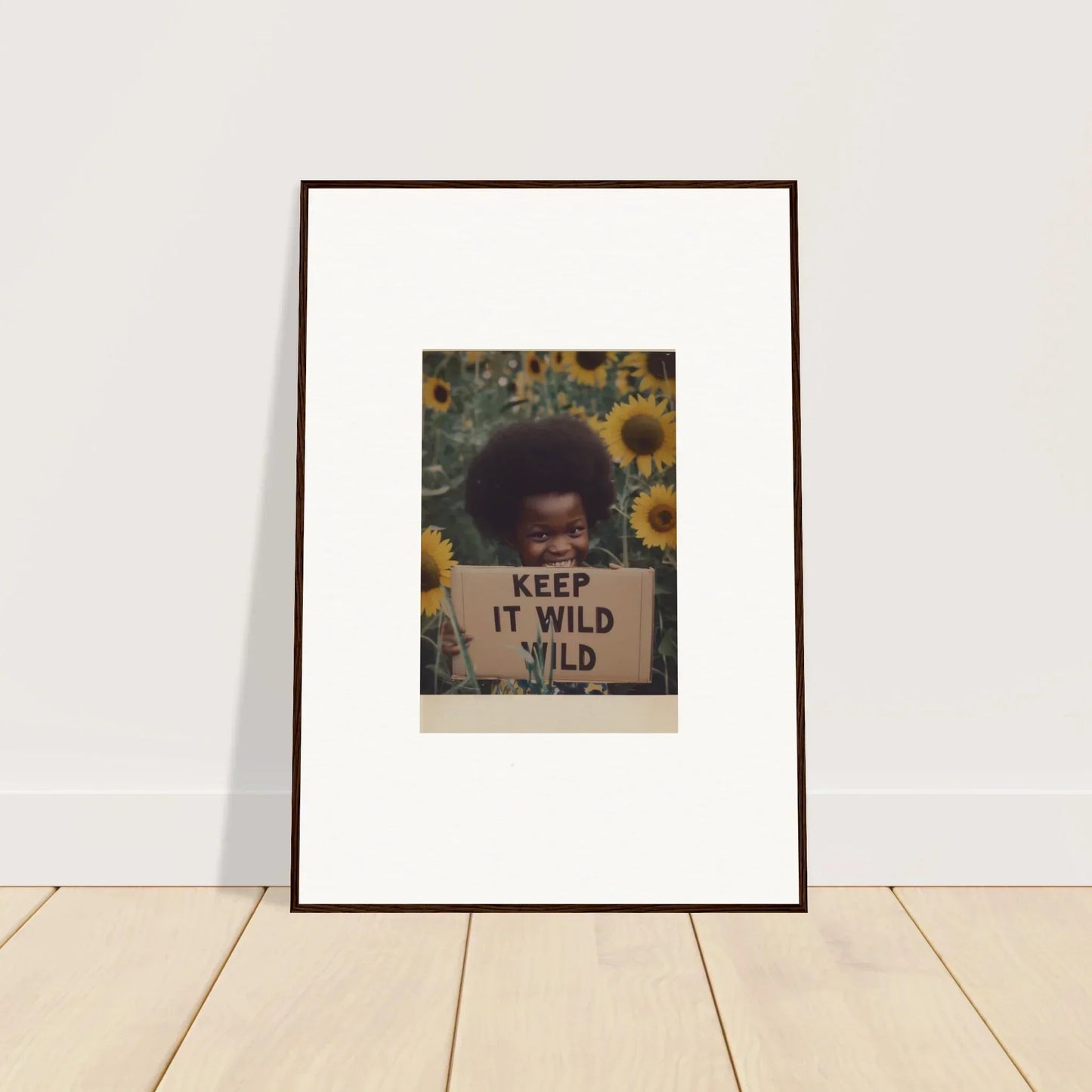 Framed photo of someone with an afro holding a KEEP IT WILD sign in sunflowers for Euphoric Sun Voyages