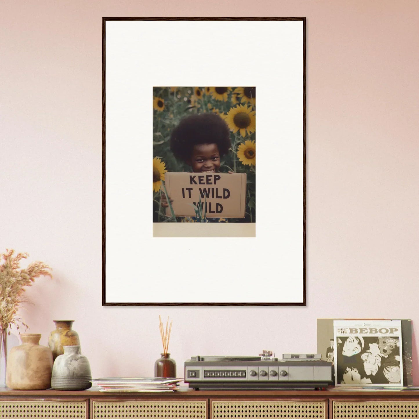 Framed photo of someone with an afro and a KEEP IT WILD sign in sunflowers for Euphoric Sun Voyages