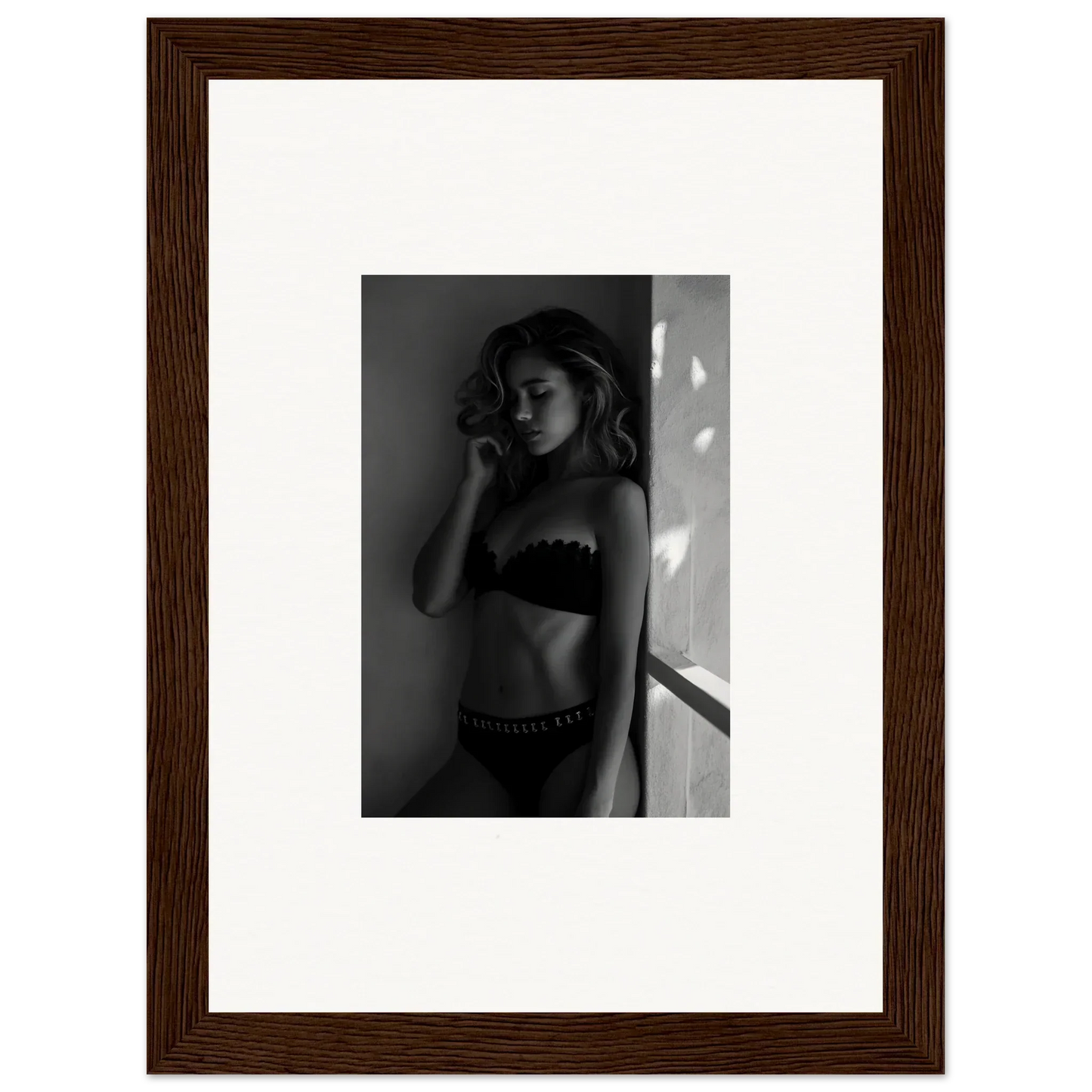 Black and white photograph of a woman in lingerie posed against a wall.