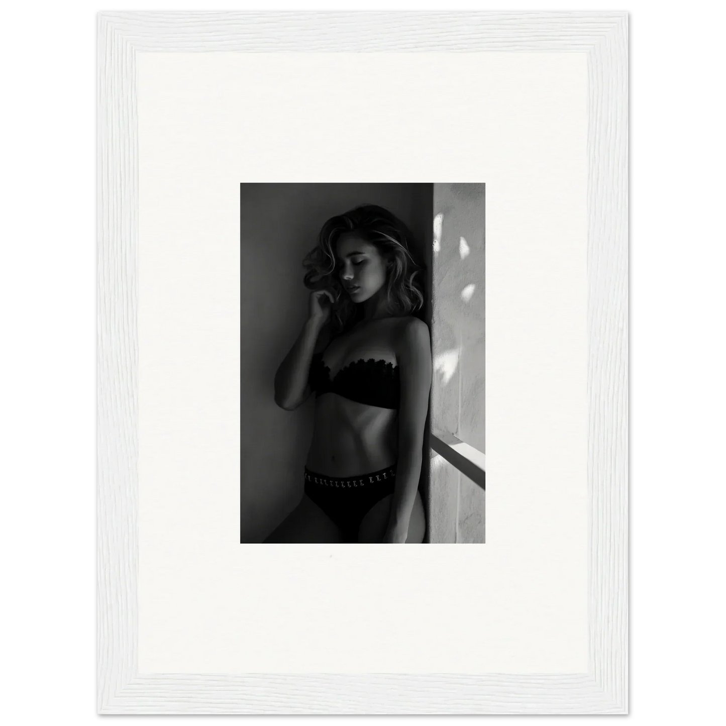 Black and white photograph of a woman in lingerie standing near a wall.