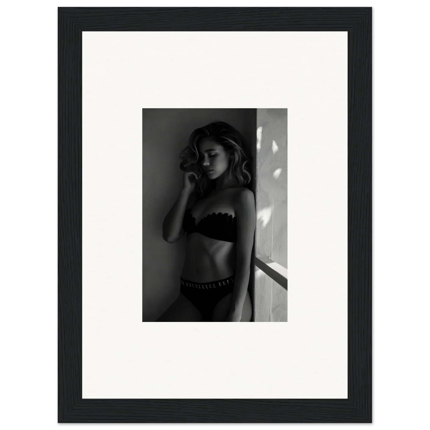 Black and white photograph of a woman in lingerie posing against a wall.