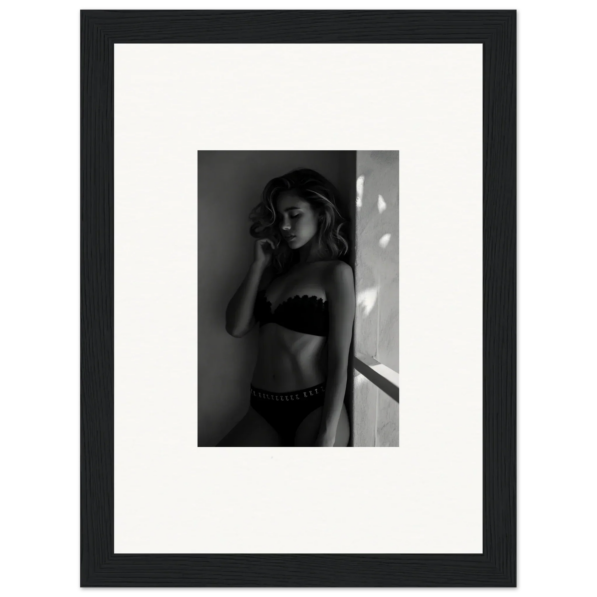 Black and white photograph of a woman in lingerie posing against a wall.