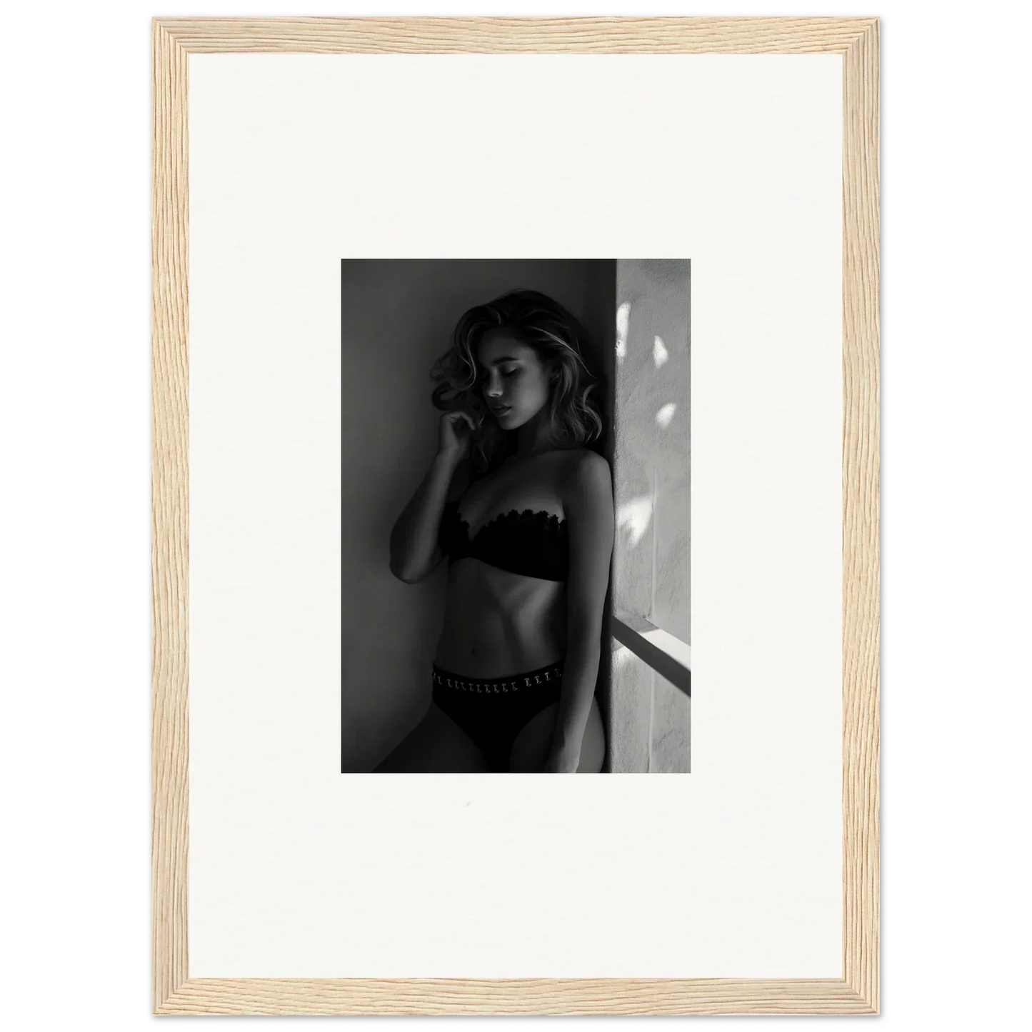 Black and white photograph of a woman in lingerie, framed in a light wooden frame.