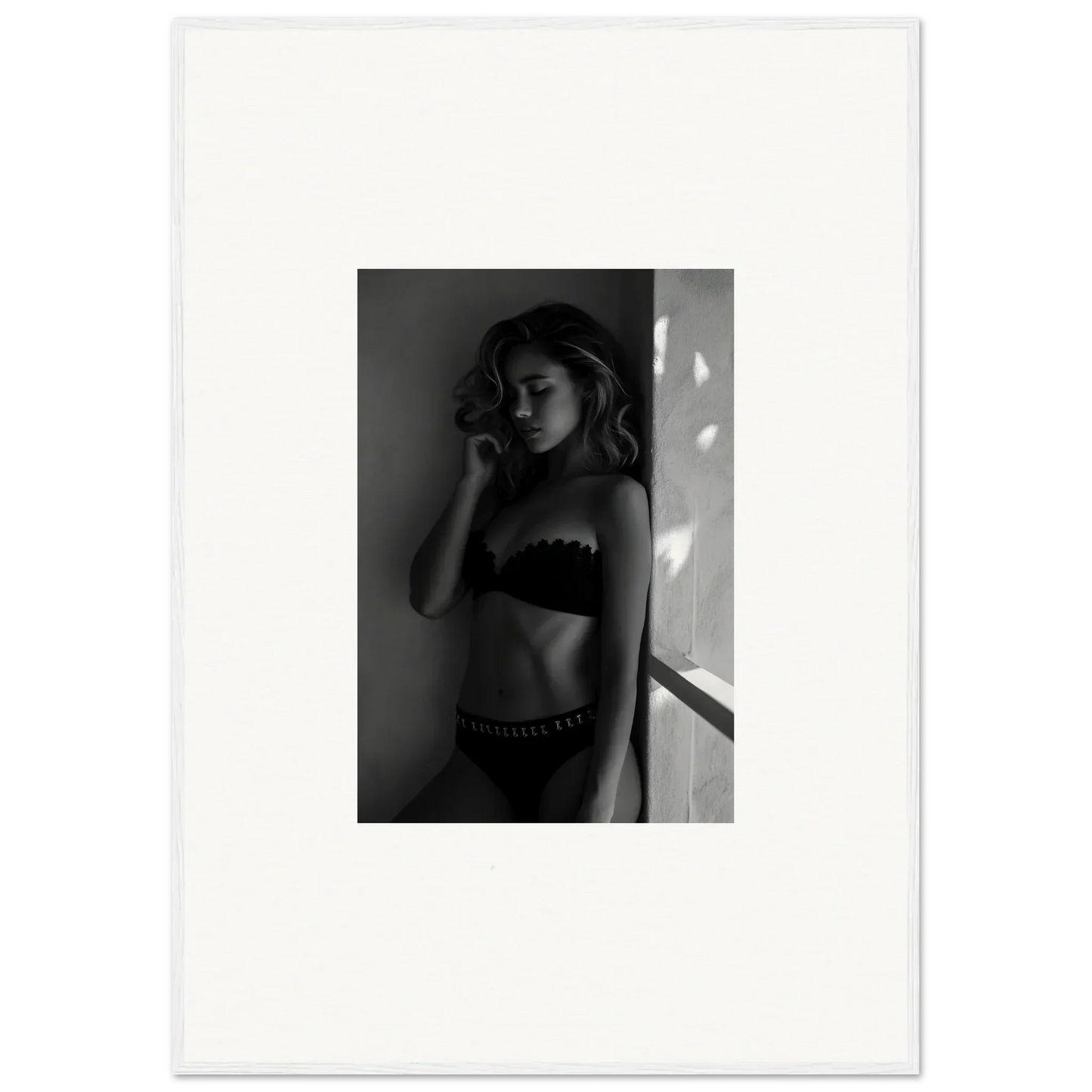 Black and white photograph of a woman in lingerie standing against a wall.