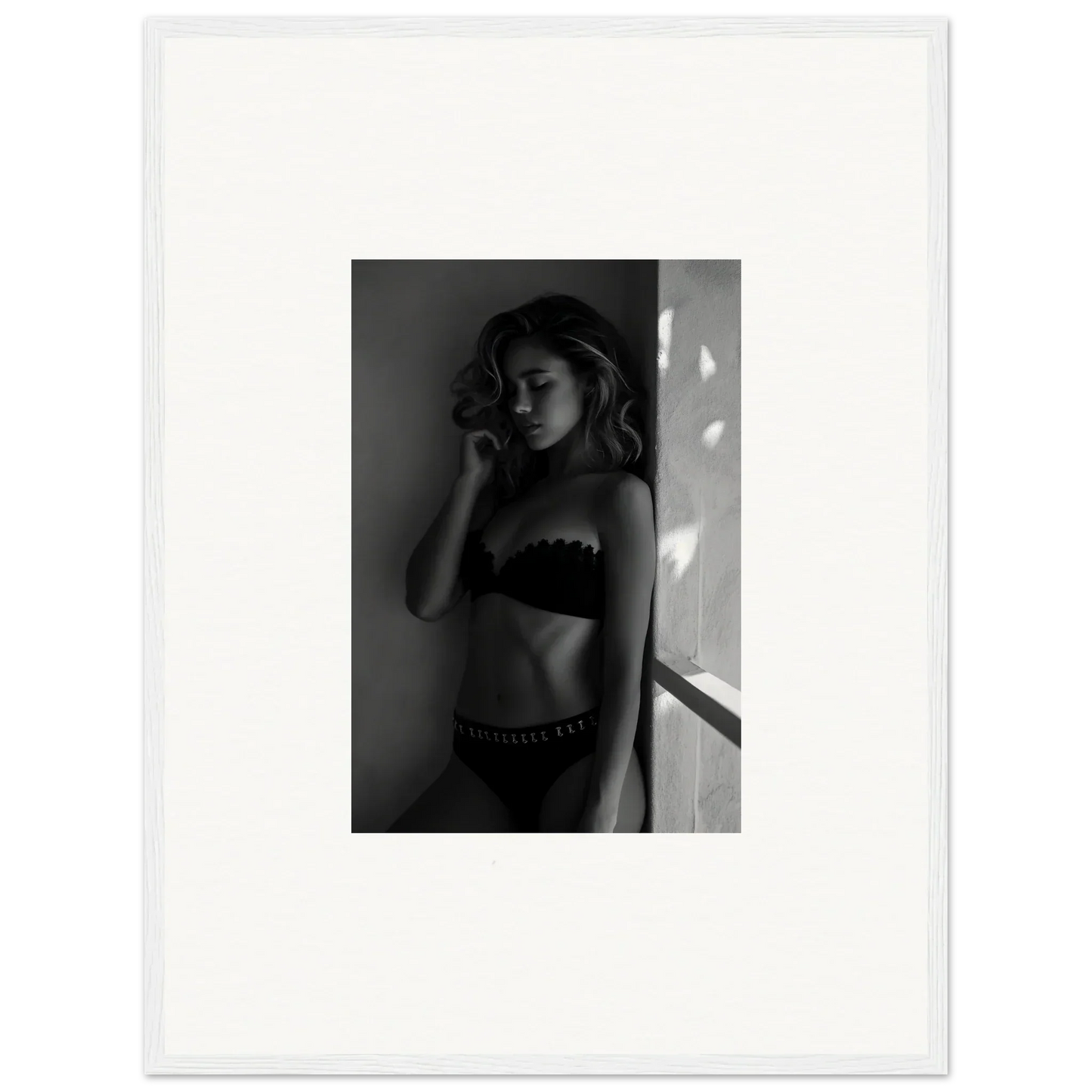 Black and white photograph of a woman in lingerie standing near a wall.