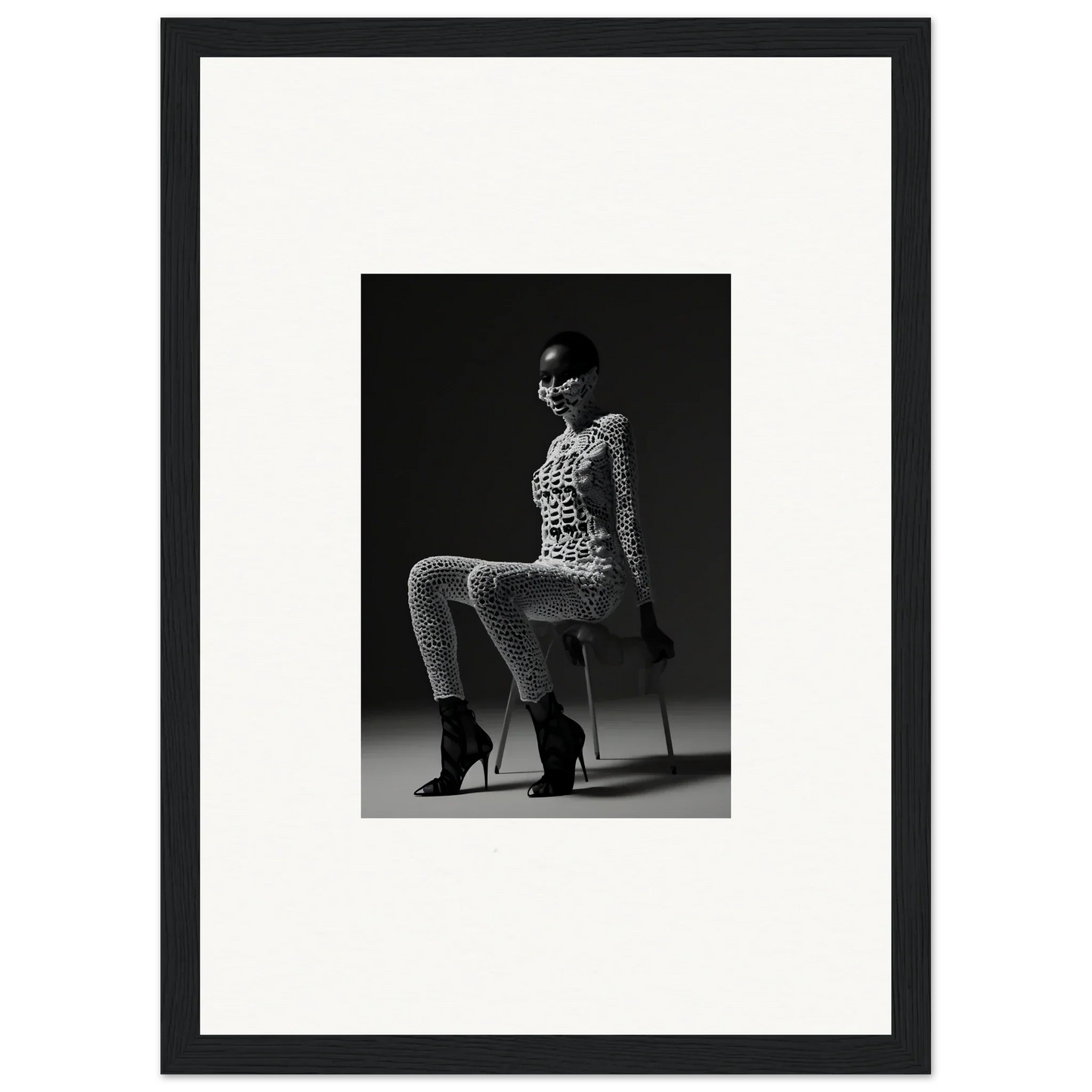 Black and white photograph of a woman seated on a stool wearing a patterned outfit and high heels.