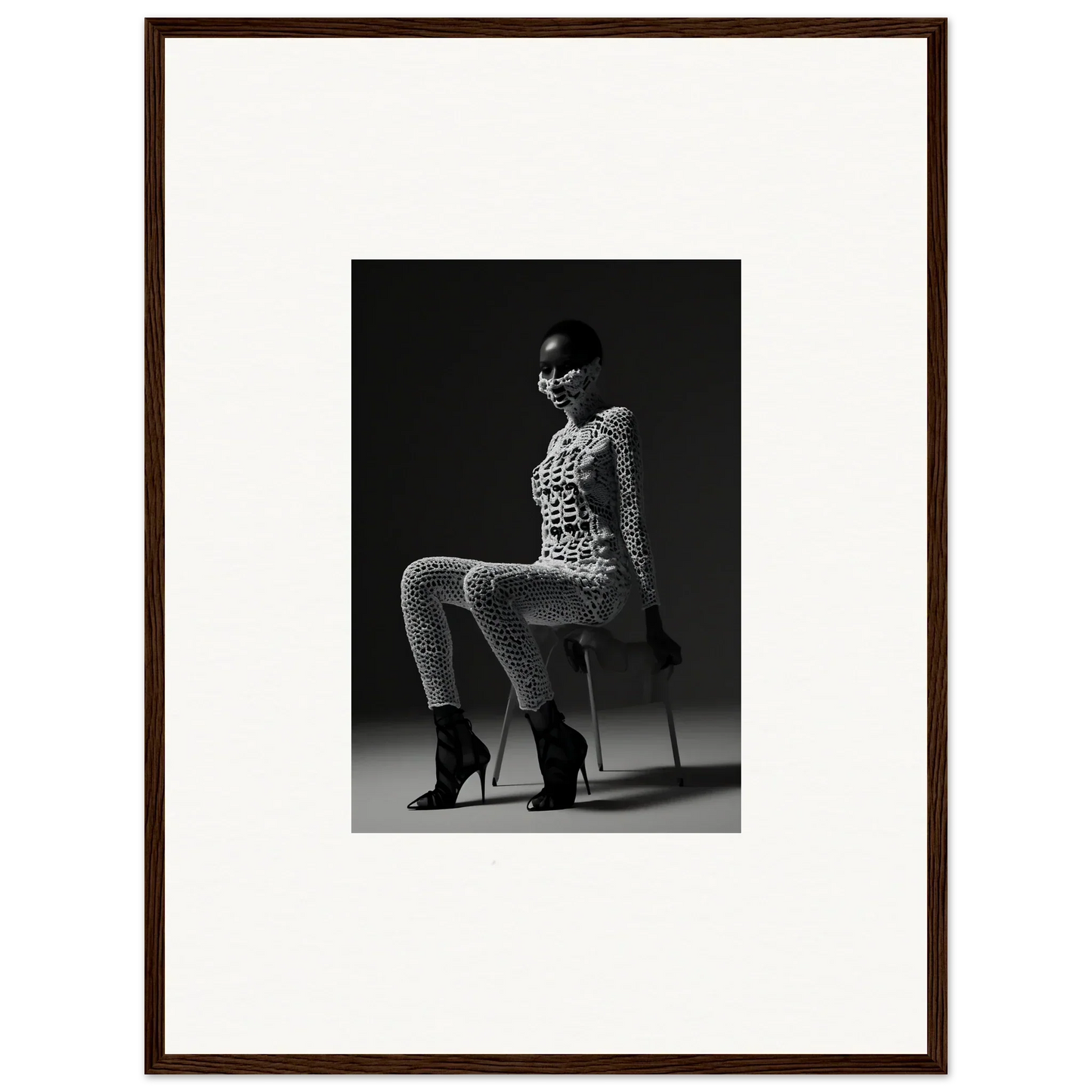 Black and white photograph of a woman in a patterned bodysuit and high heels posing on a stool.