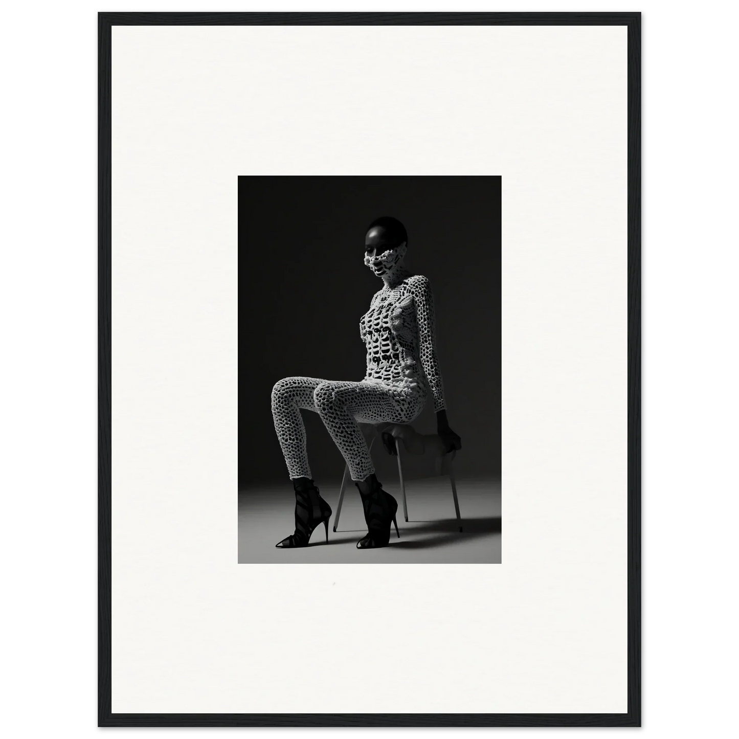 Black and white photograph of a woman in a patterned bodysuit and high heels sitting on a stool.