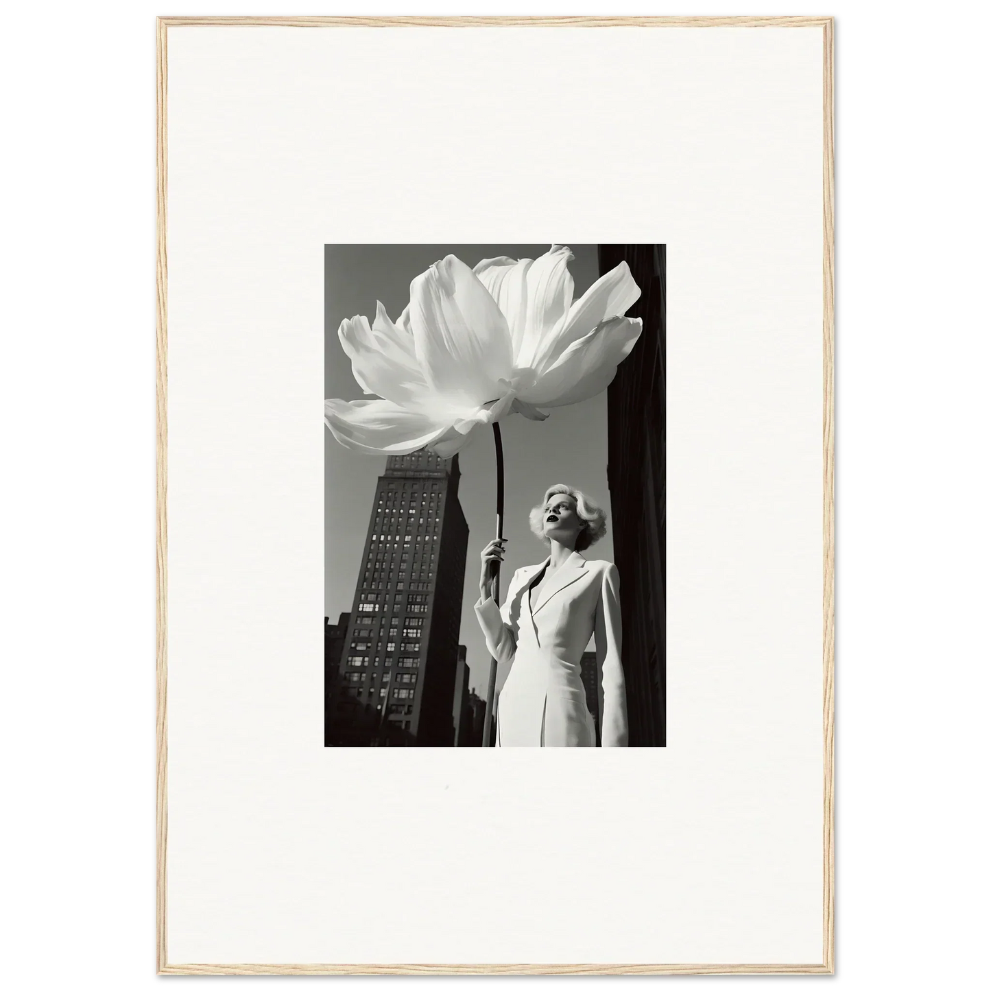 Black and white photograph of a woman standing next to an oversized flower sculpture against a cityscape backdrop.