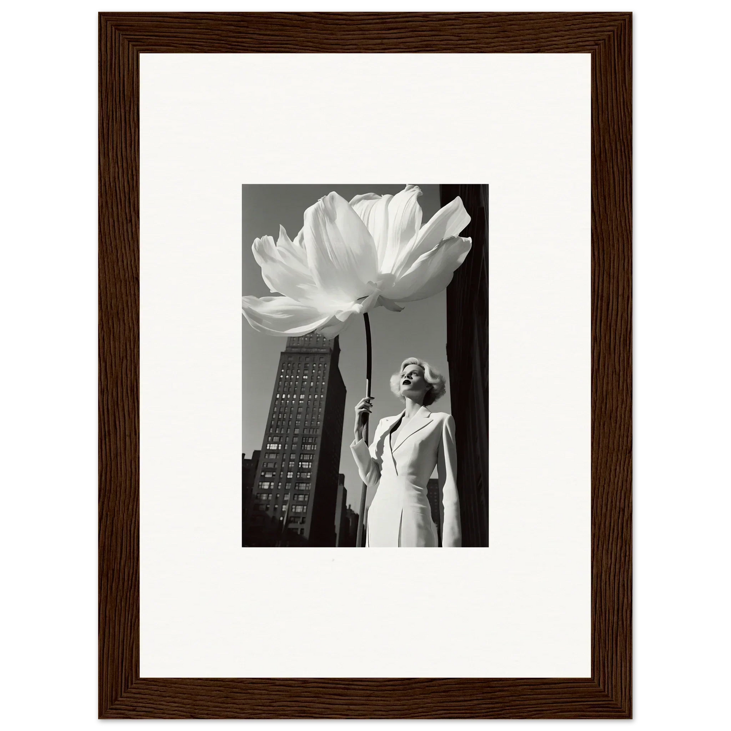 Framed black and white photograph showing a person standing next to an oversized flower in an urban setting.