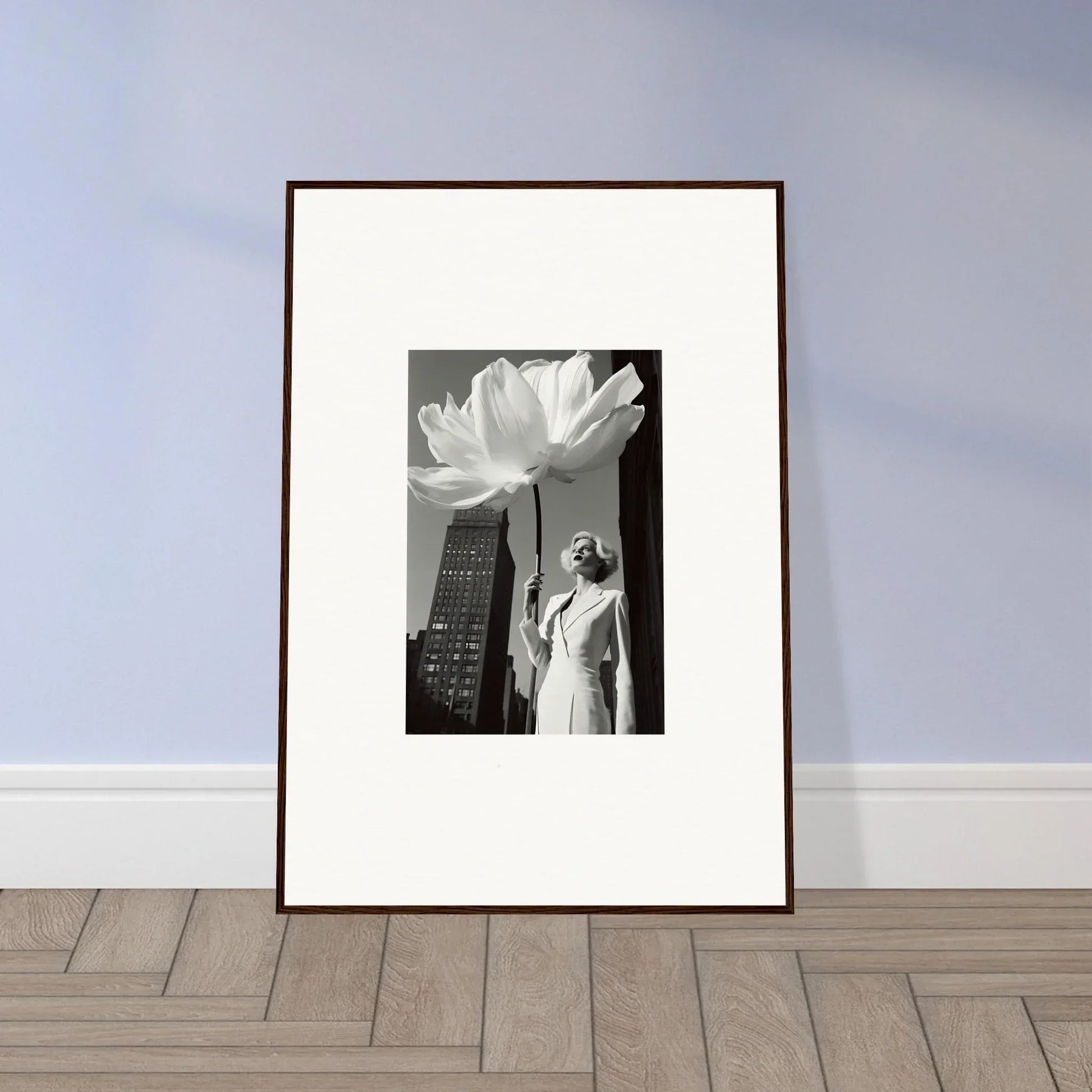 Framed black and white photograph showing a figure beneath a giant flower with a skyscraper in the background.