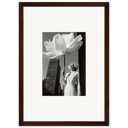 A framed black and white photograph showing a person standing next to an oversized flower against a cityscape backdrop.