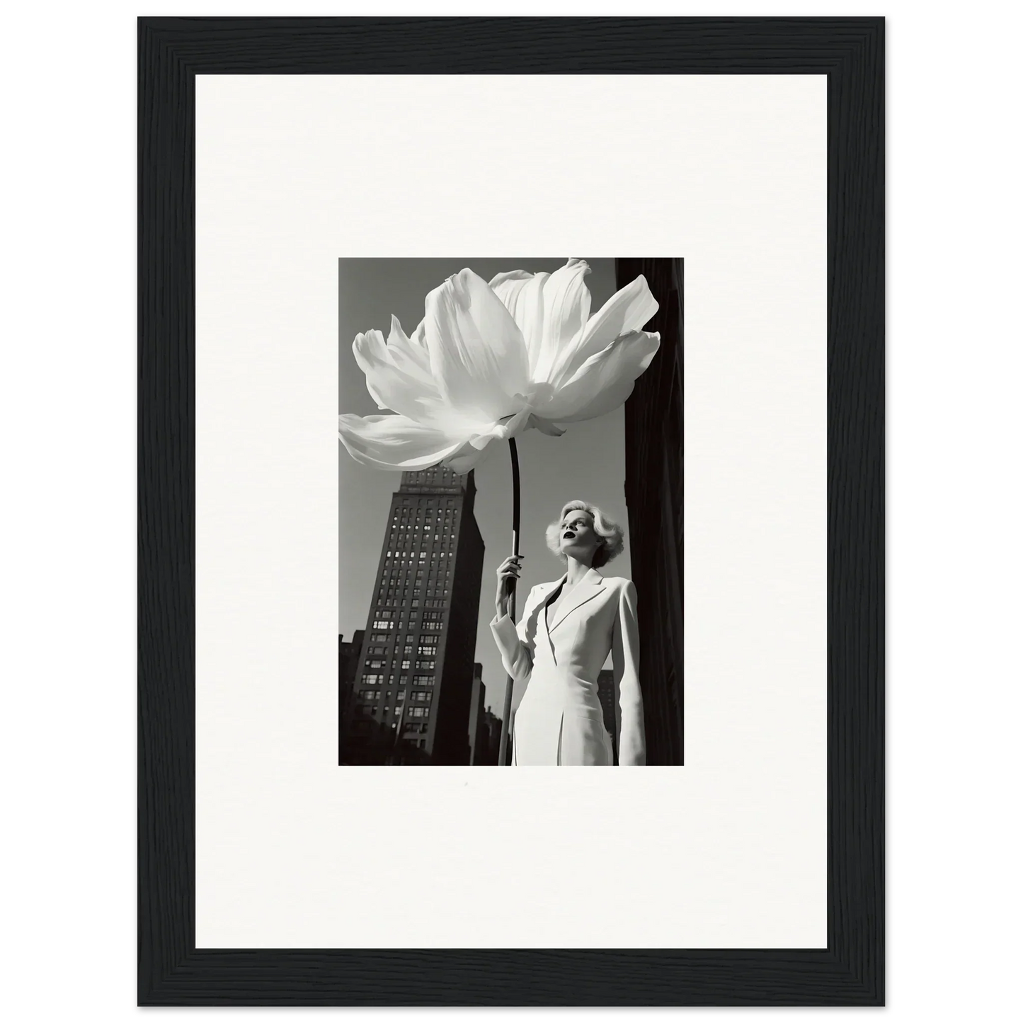 Black and white photograph of a woman standing next to an oversized flower in an urban setting.